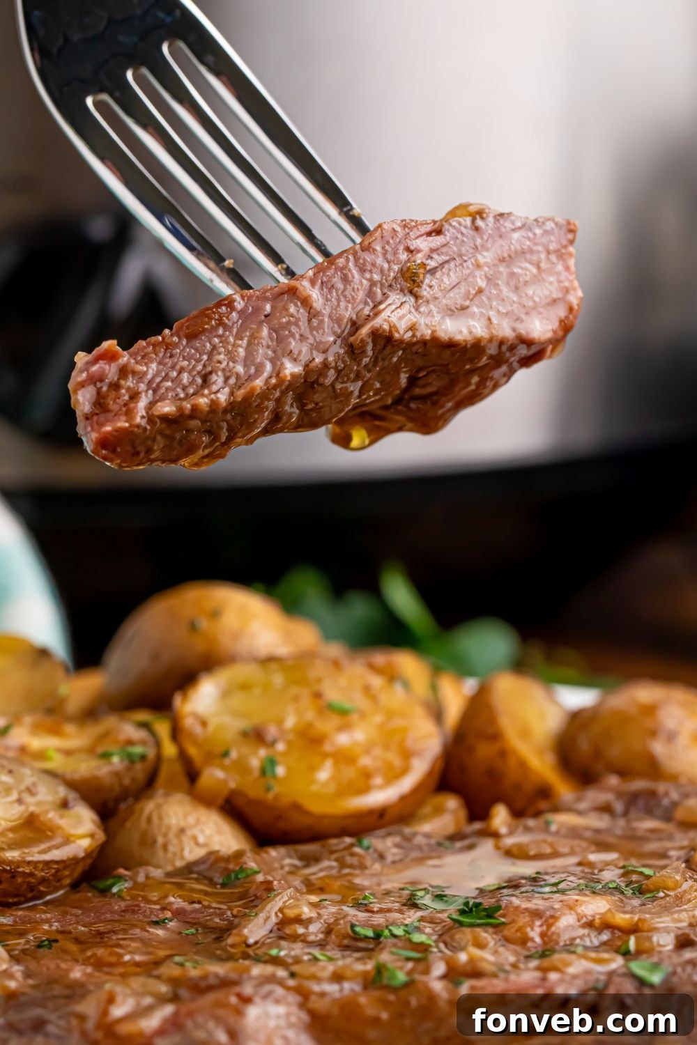 A slice of tender steak on a fork above a full plate of Crock Pot Steak and Potatoes