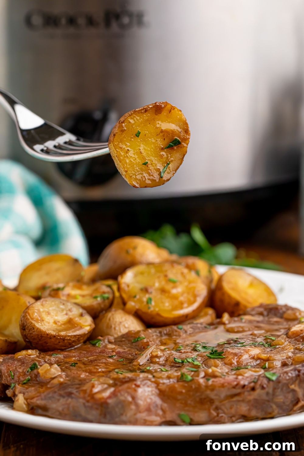 A fork holding a tender potato, poised above a plate of Crock Pot Steak and Potatoes