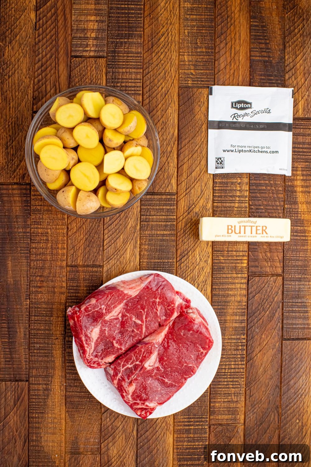 Ingredients for Crock Pot Steak and Potatoes laid out on a wooden table, including steak, potatoes, and soup mix