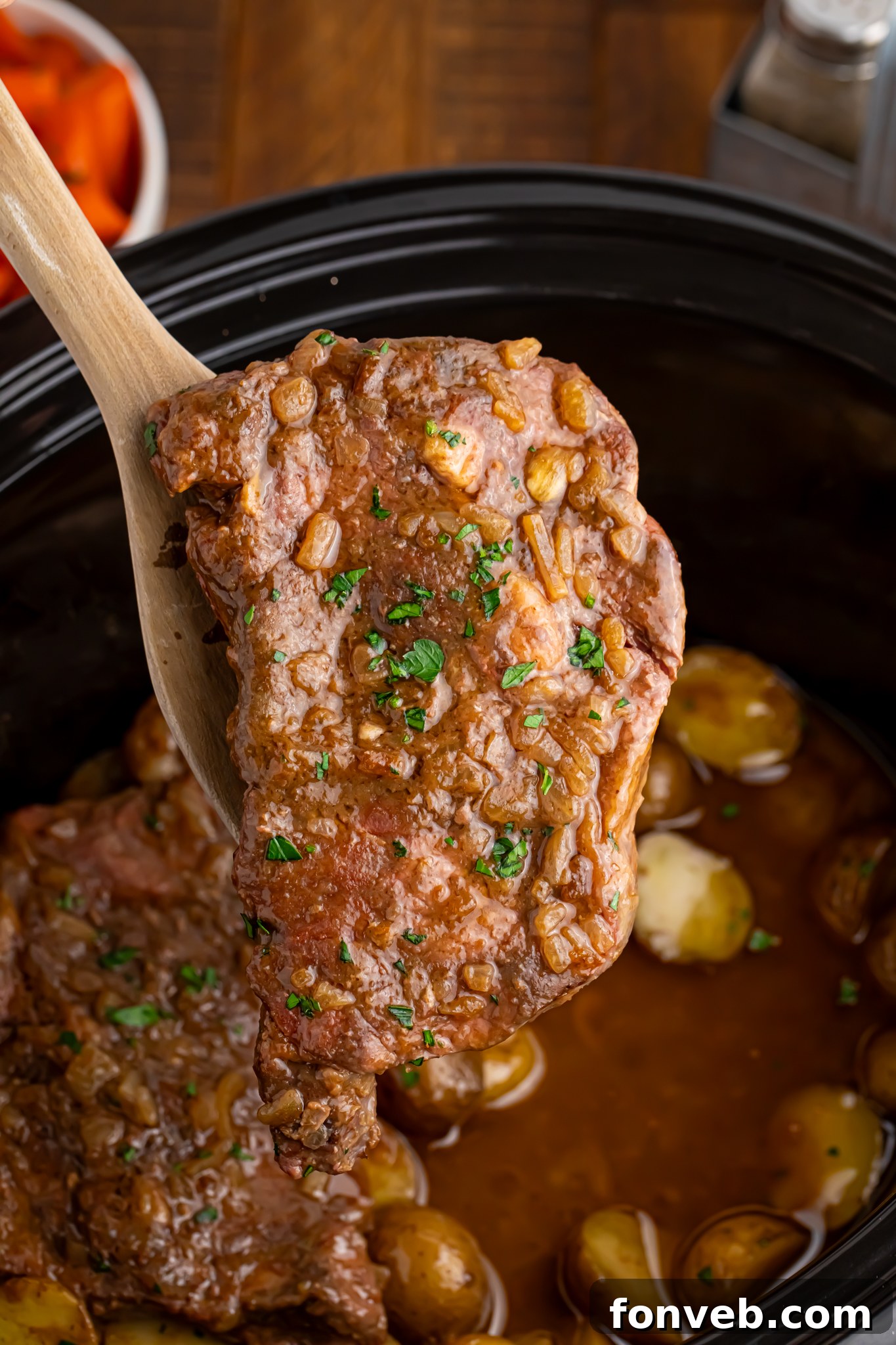 Tender Crock Pot Steak being gently lifted out of the slow cooker with a wooden spoon