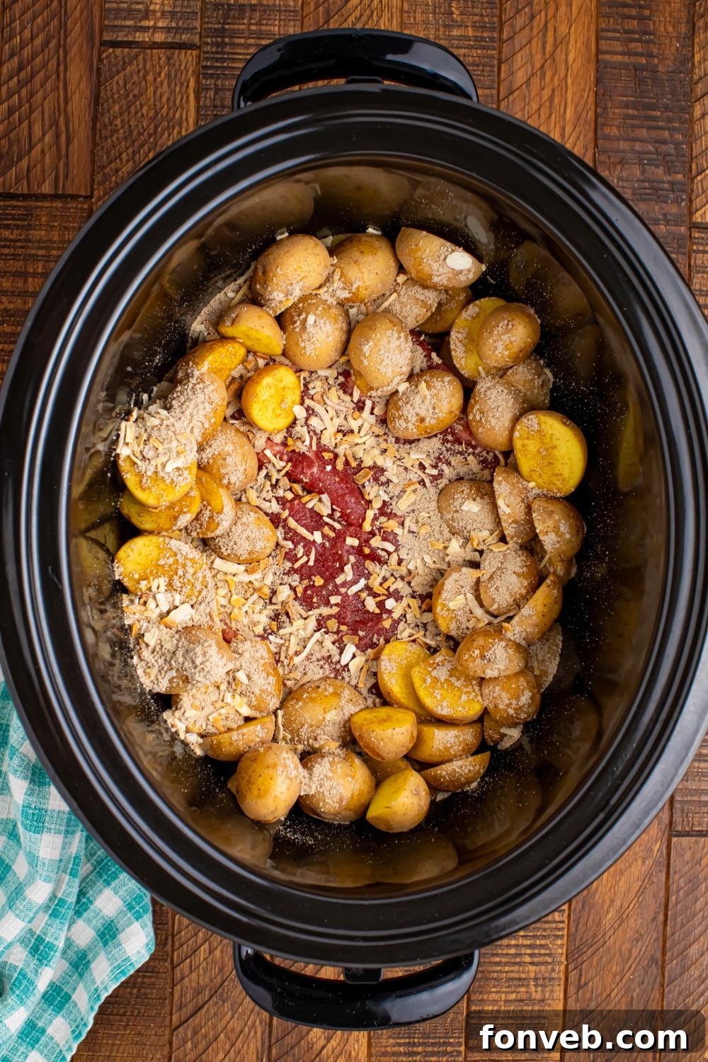 Seasoning being sprinkled over potatoes and steak in the crock pot