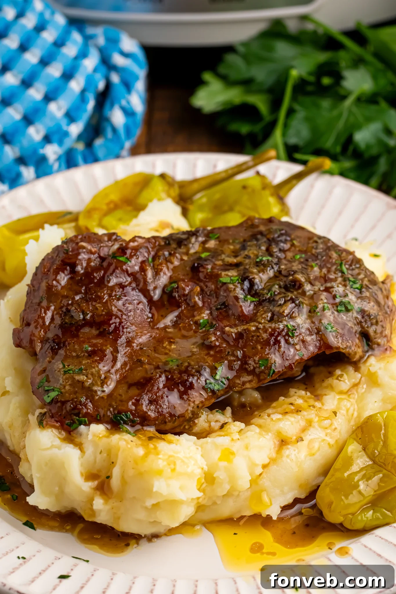 Slow Cooker Mississippi Ribeye Steaks on a white plate, on top of fluffy mashed potatoes
