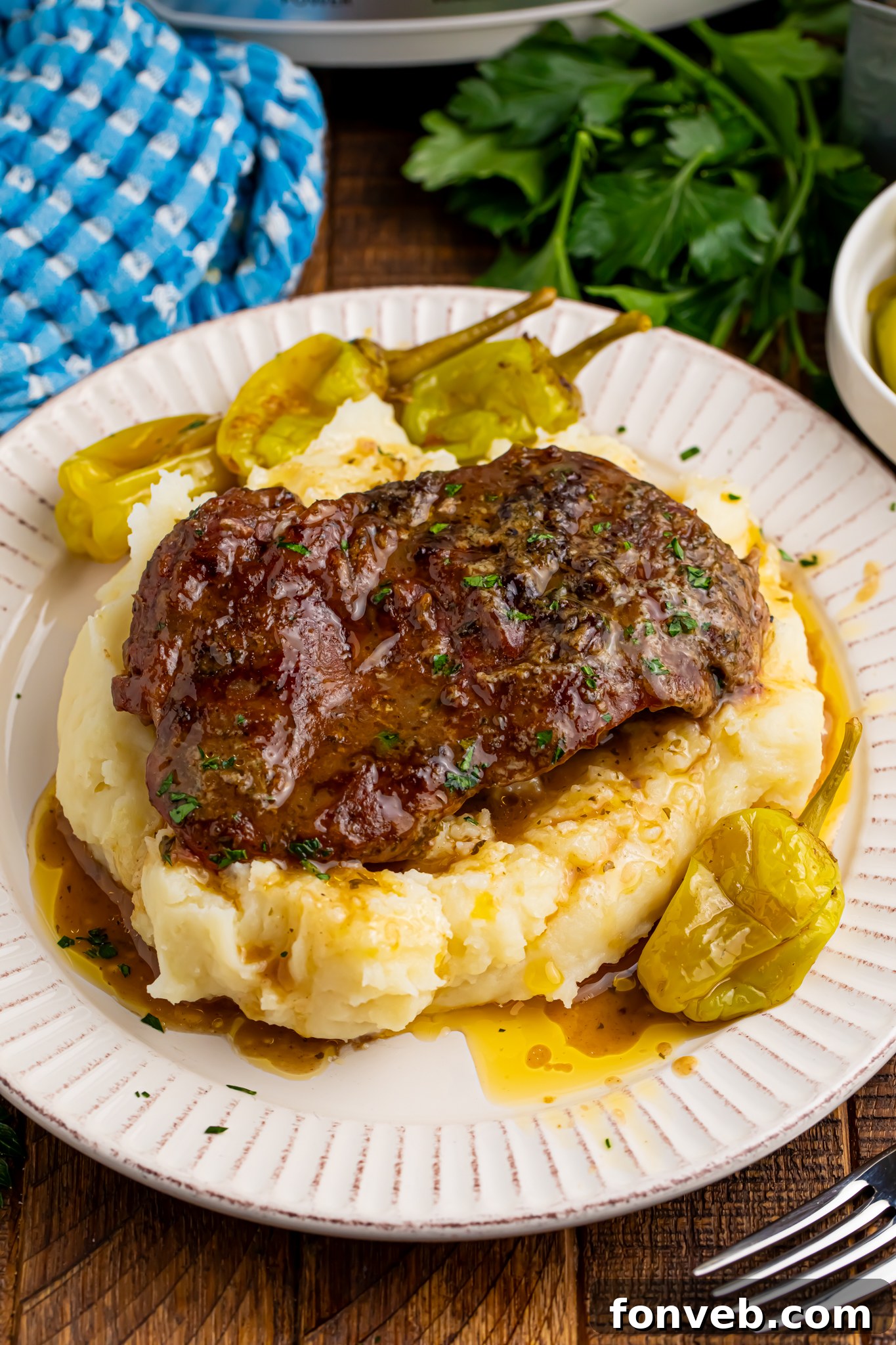 Slow Cooker Mississippi Ribeye Steaks on a white plate, on top of fluffy mashed potatoes with gravy on top