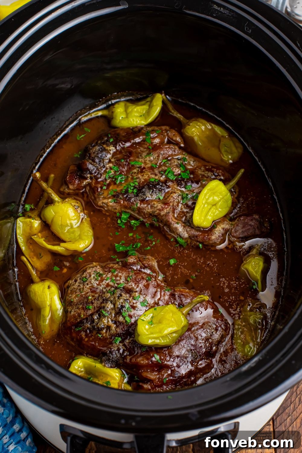Slow Cooker Mississippi Ribeye Steaks sitting in a crockpot wih peppers on top