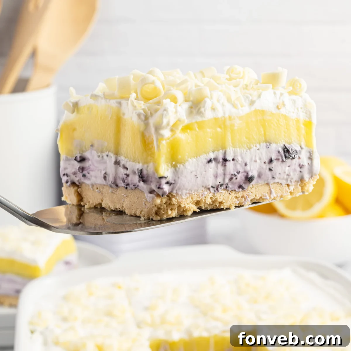Piece of Lemon Blueberry Lush being lifted out of a white baking pan, showcasing its beautiful layers.