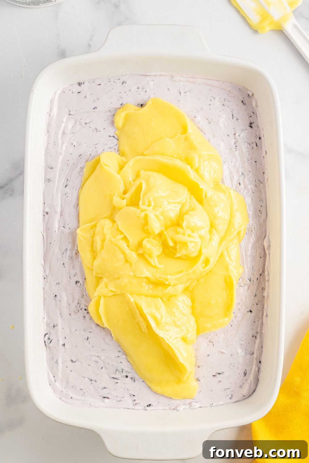 Spreading the lemon pudding layer evenly over the blueberry cream cheese layer in the baking pan.