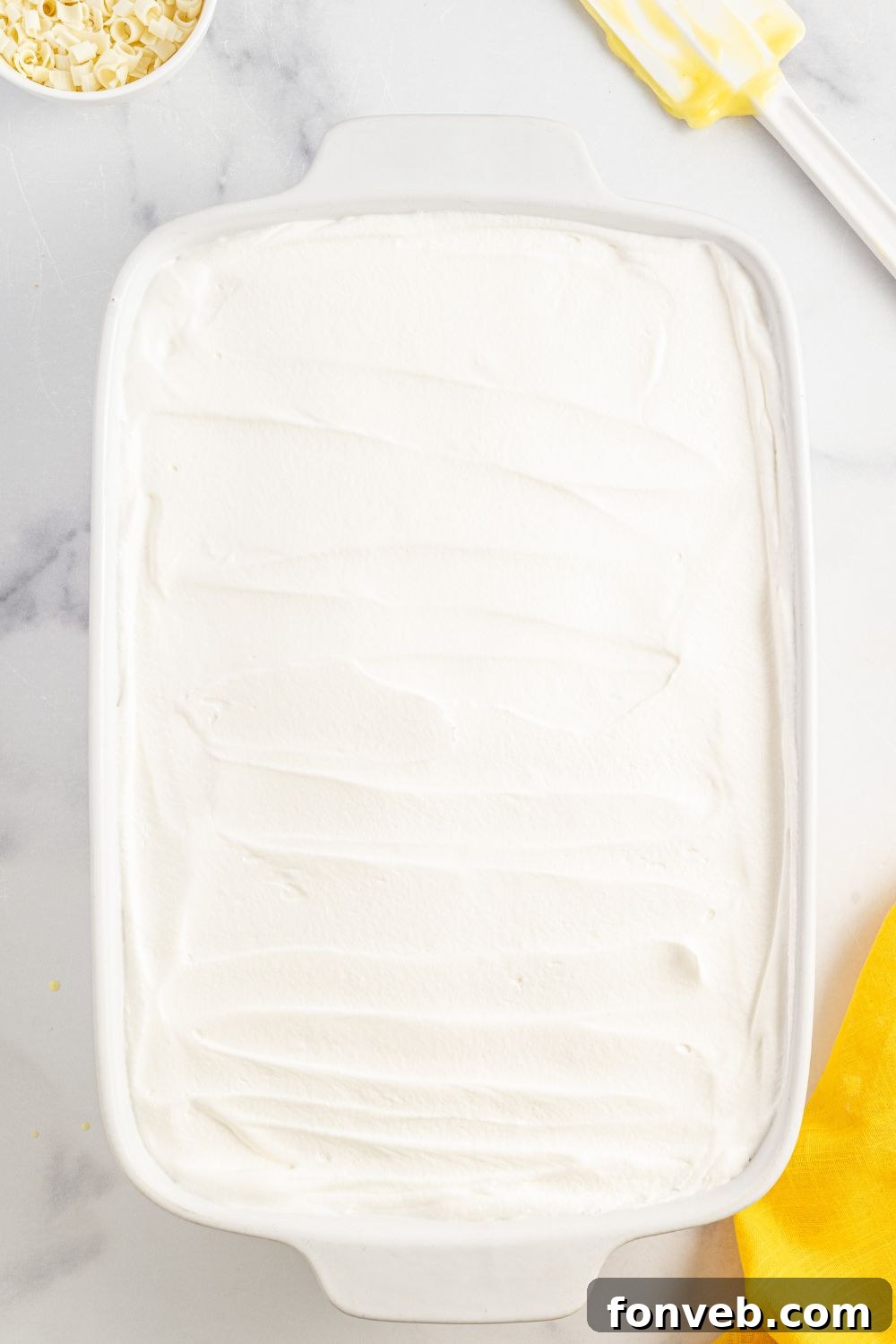Whipped cream topping spread smoothly over the lemon pudding layer of the Lemon Blueberry Lush dessert in the pan.