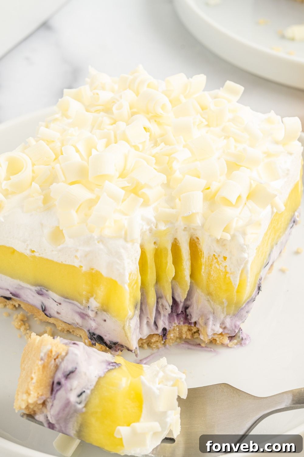 Lemon Blueberry Lush dessert sitting on a plate with a fork, showing a bite already taken out, highlighting the layers.