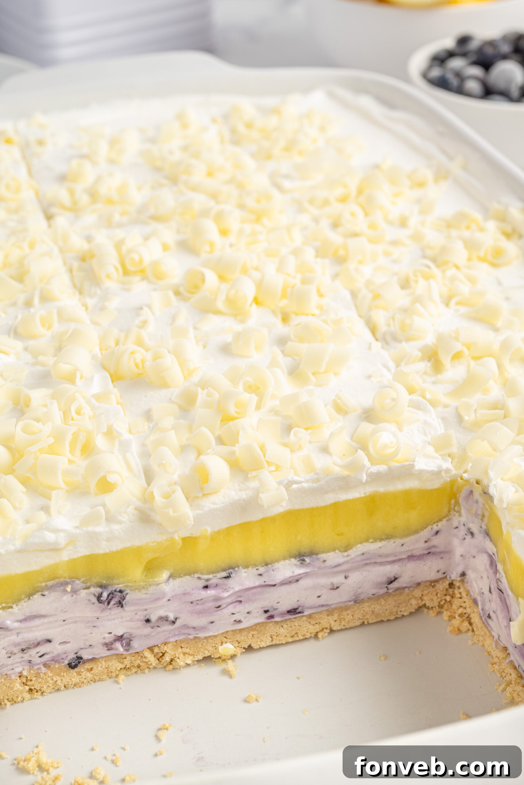 Close-up view of the distinct layers of Lemon Blueberry Lush in the baking pan, with a few slices already removed.