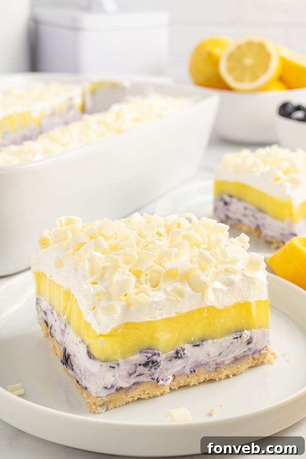 A slice of blueberry delight dessert on a plate, with more slices arranged around it on a table, ready to be served.