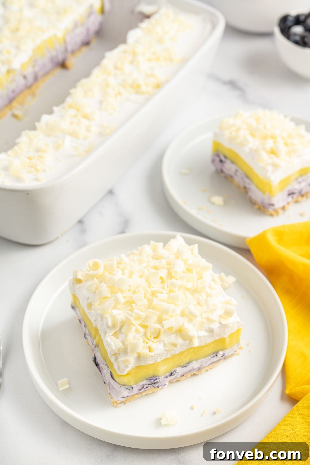 Blueberry lemon lasagna slices on plates, with the full dish visible in the background, ready for serving.