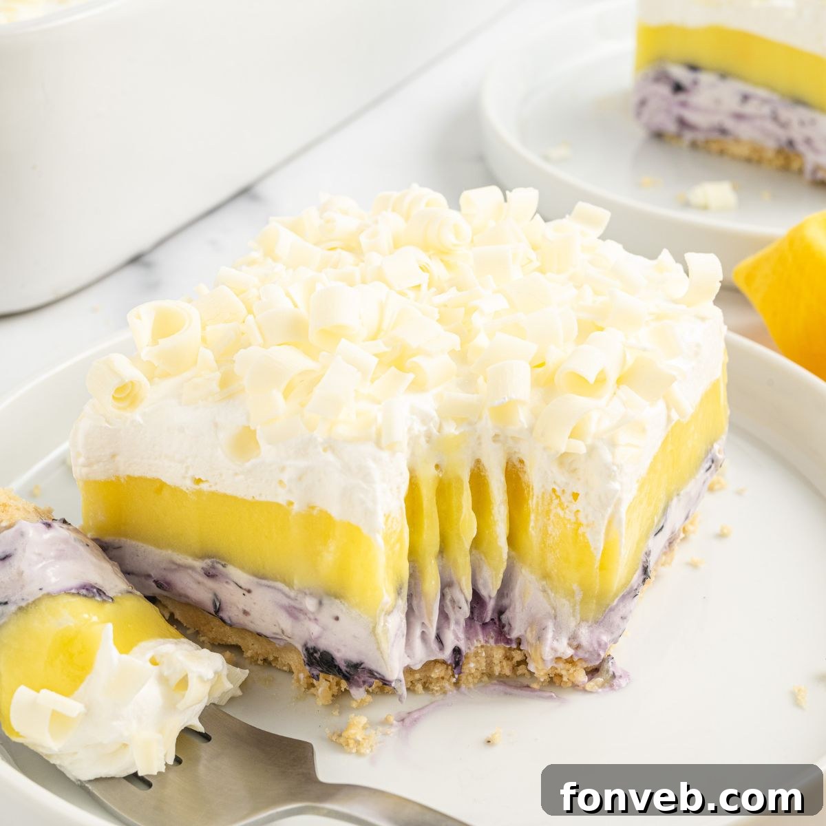 Lemon Blueberry Lush dessert sliced on a white plate with a fork taking a bite, showing the rich texture.