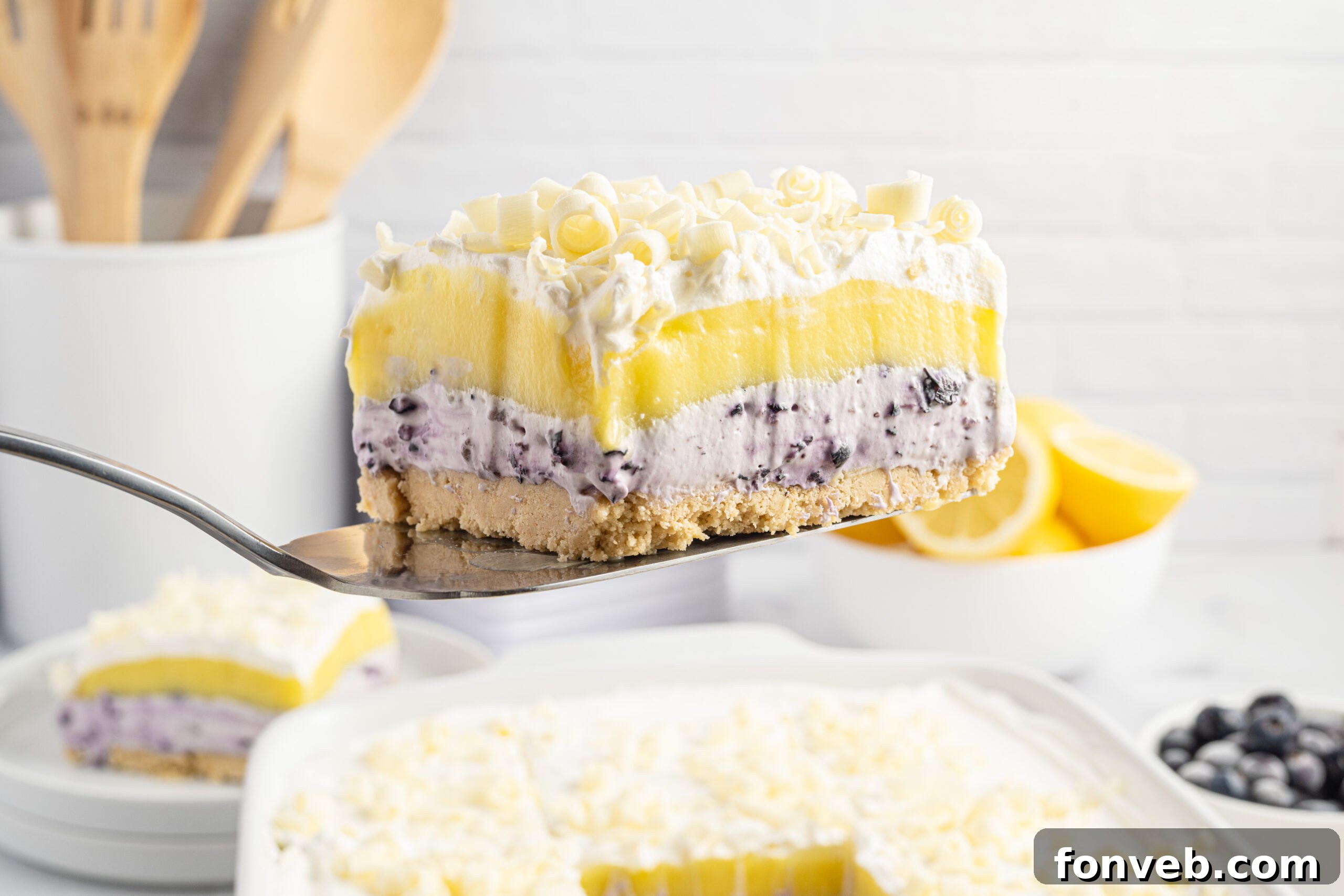 A piece of Lemon Blueberry Lush dessert being lifted out of a white baking pan, ready to be served.