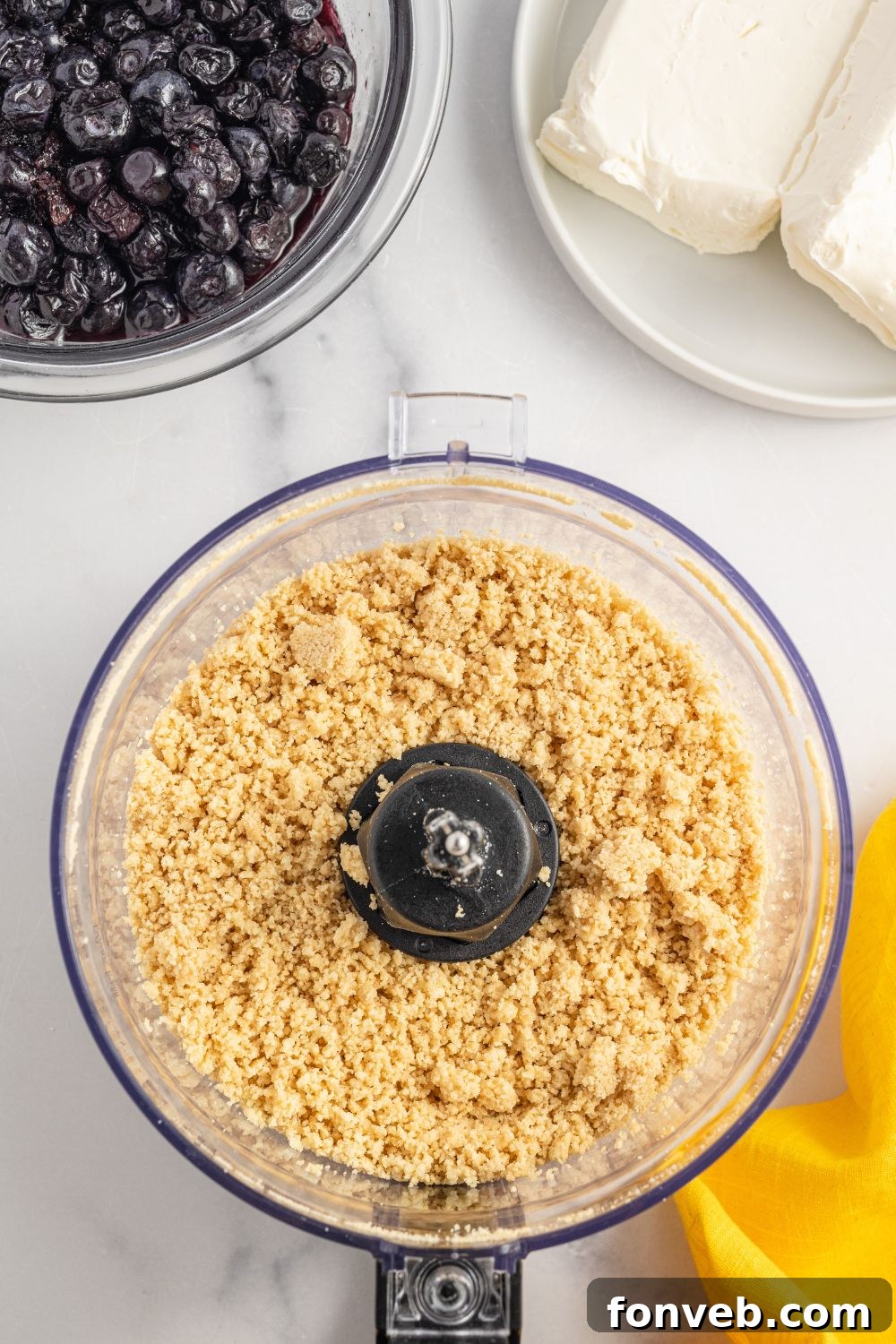 Crushed golden oreo cookies in a food processor on a table.