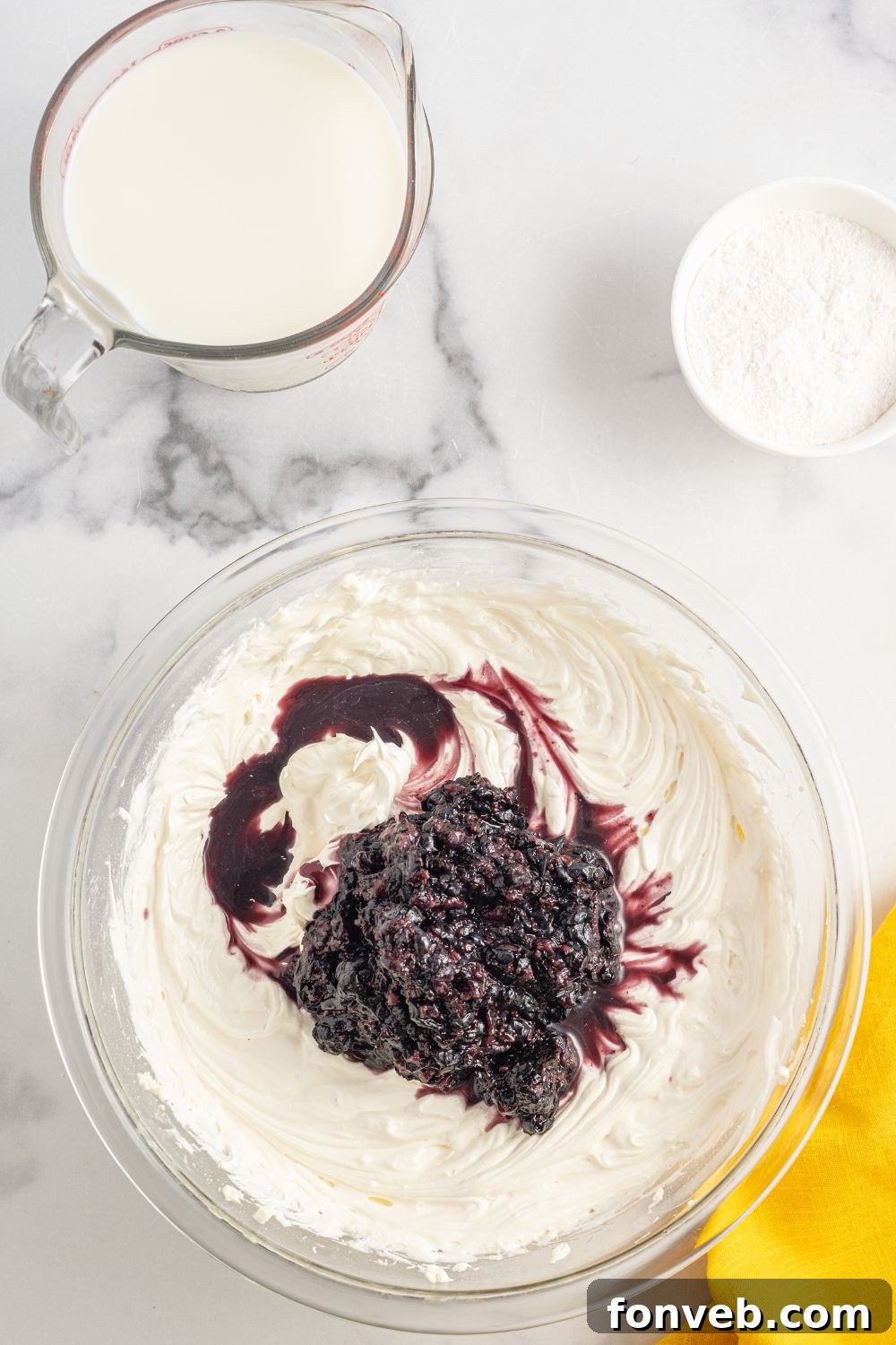 Cream cheese and blueberry mixture in a bowl, sitting on a table with other ingredients, showing its smooth texture.