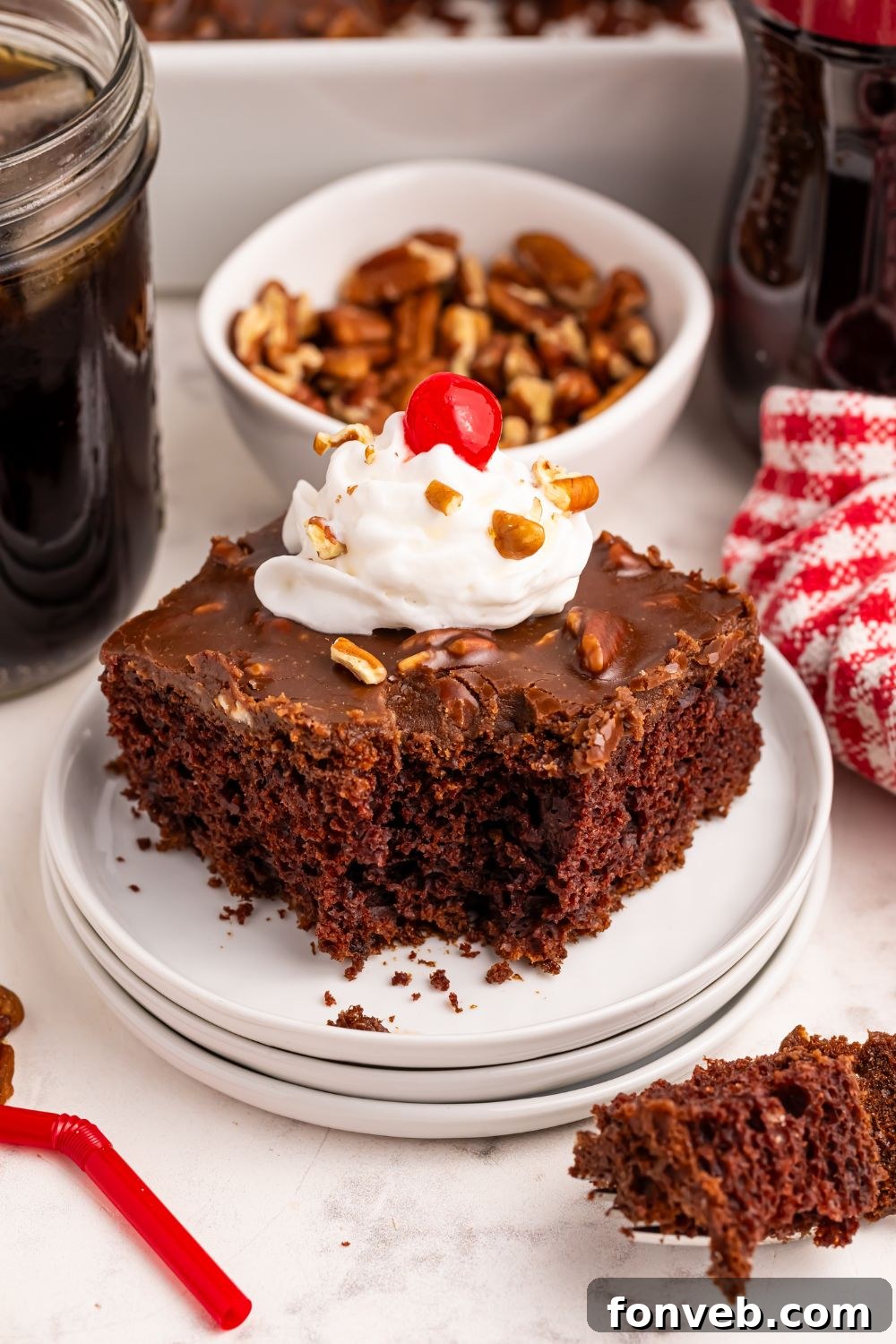 Classic Dr. Pepper Cake 2 A slice of Dr. Pepper Cake on a white plate, topped with a dollop of whipped cream and a bright red cherry. A bite has been taken, revealing the moist chocolate crumb.