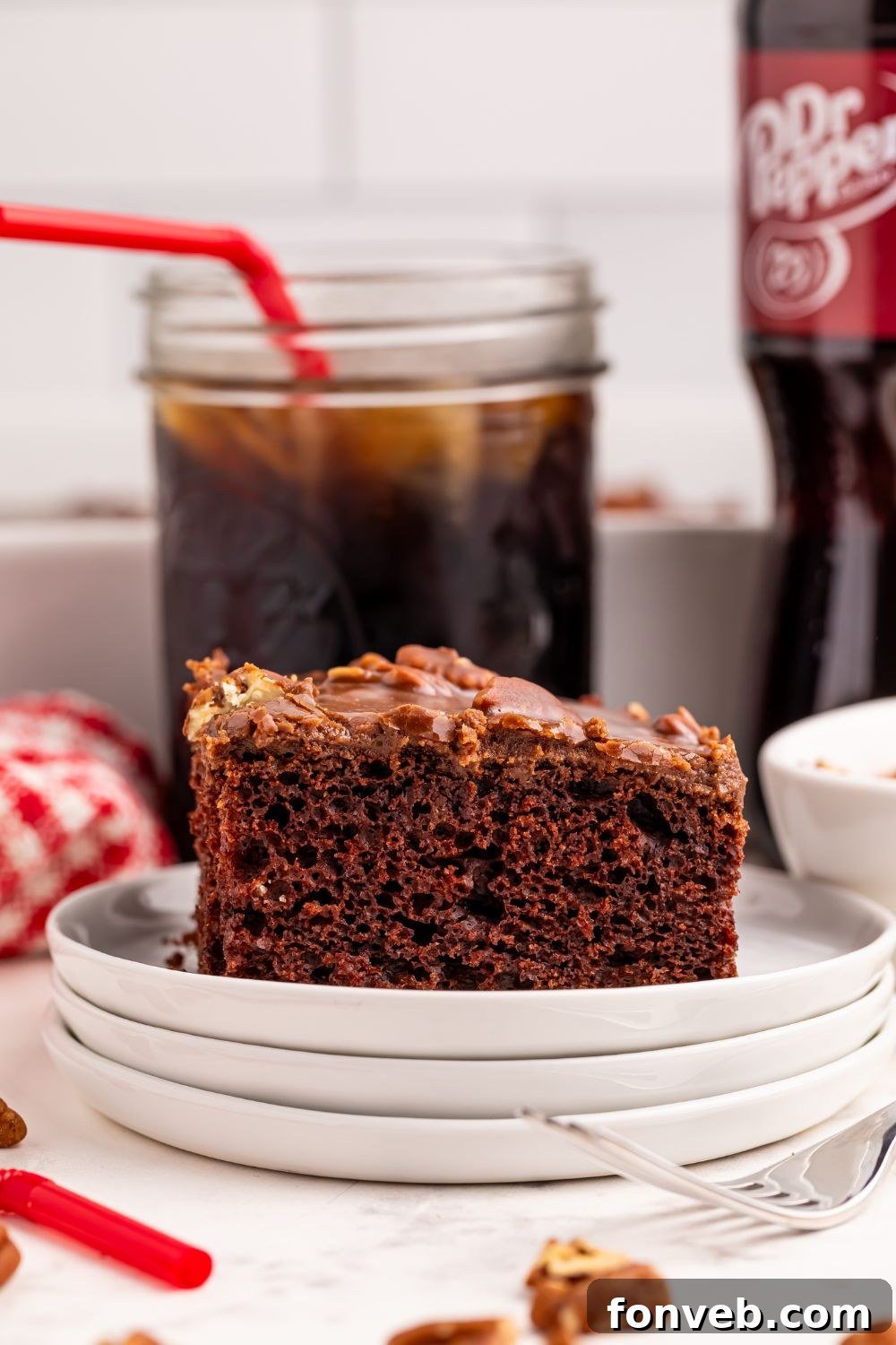 Classic Dr. Pepper Cake 16 A tantalizing slice of Dr. Pepper Cake on a white plate, with a vintage mason jar filled with Dr. Pepper sitting behind it on a wooden table.