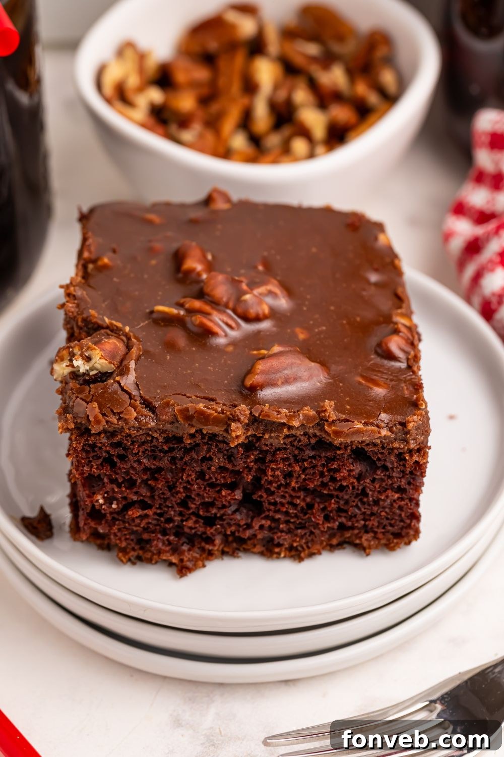 Classic Dr. Pepper Cake 20 A slice of Dr. Pepper Cake on a white plate, with a rustic wooden bowl full of walnuts positioned behind it on a table.