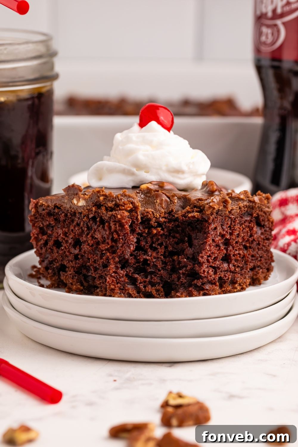 Classic Dr. Pepper Cake 5 A beautifully decorated Dr. Pepper Chocolate Cake, topped with whipped cream and a cherry, sits on a stack of white plates, ready for a special occasion.
