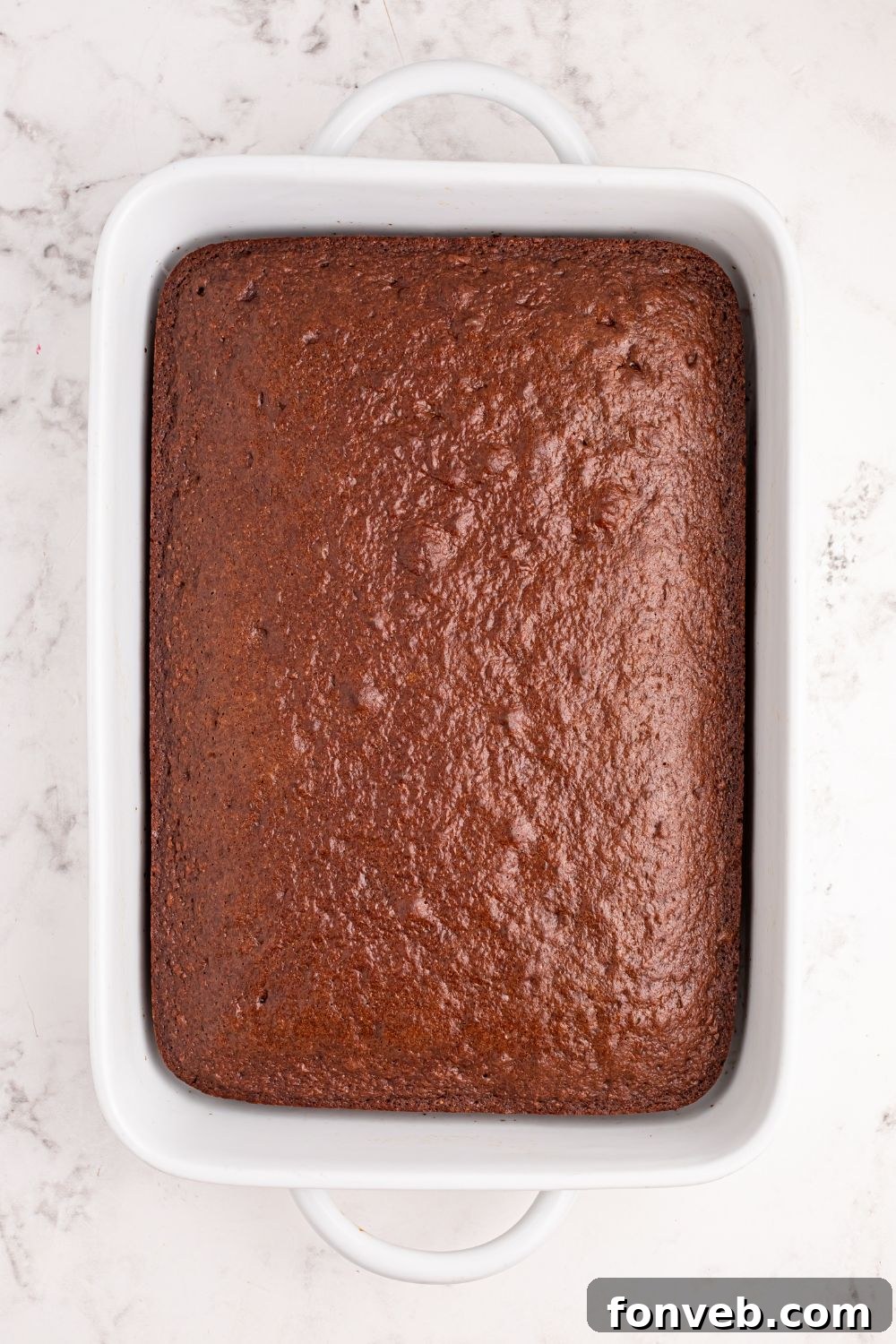 Classic Dr. Pepper Cake 7 A perfectly baked chocolate cake resting in its pan on a marble countertop, golden-brown and ready for frosting.