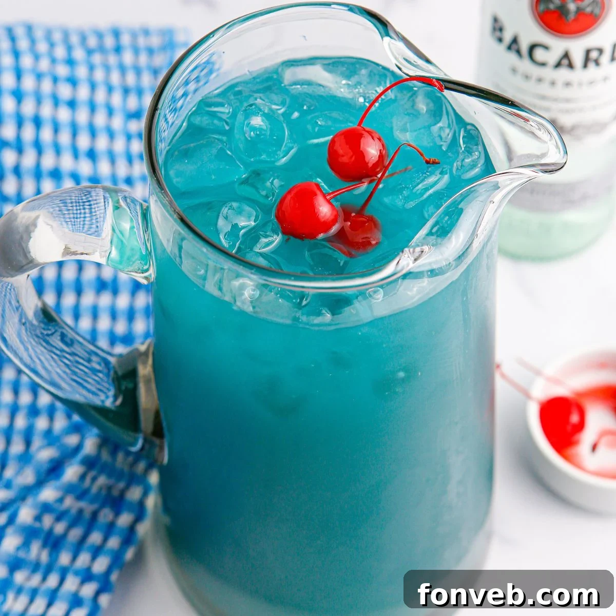 A vibrant pitcher of Blue Hawaiian Punch on a table, garnished with fresh cherries. A bottle of white rum is visible in the background, hinting at the adult nature of the drink.
