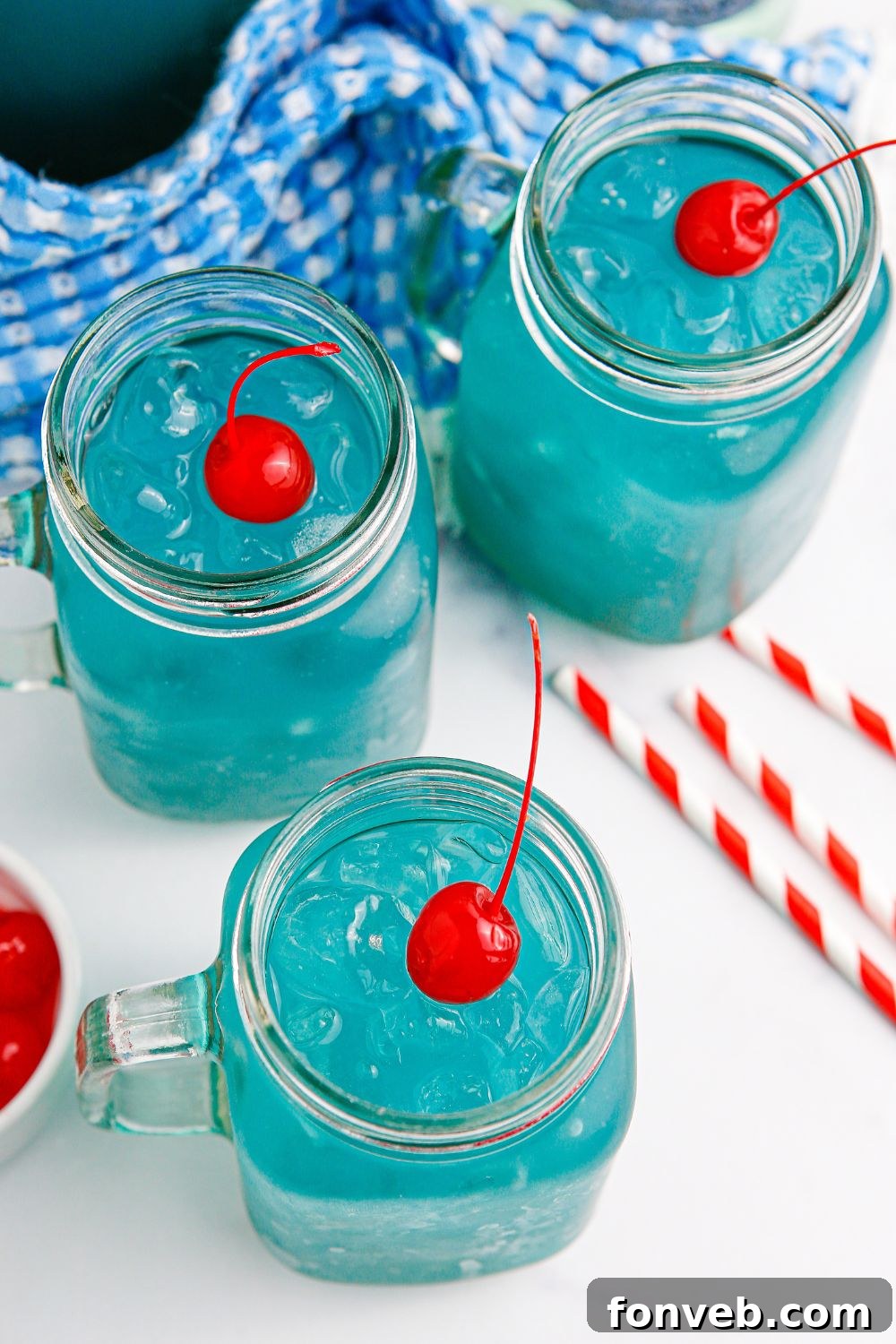Multiple glasses of the dazzling blue drink, each topped with a single red cherry on a bed of ice.