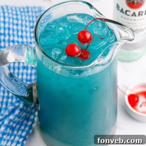A large pitcher of Boozy Blue Hawaiian Punch on a table, ready to be served, with cherries and a rum bottle in the background.