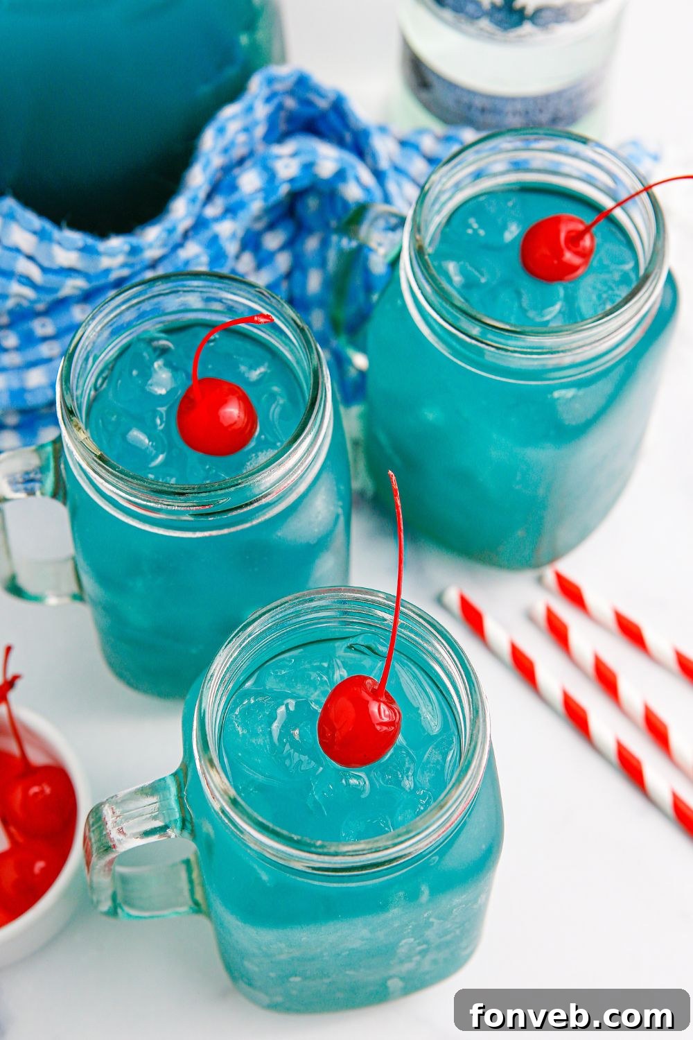 Individual glasses filled with the vibrant blue cocktail, each topped with a bright red cherry on ice.