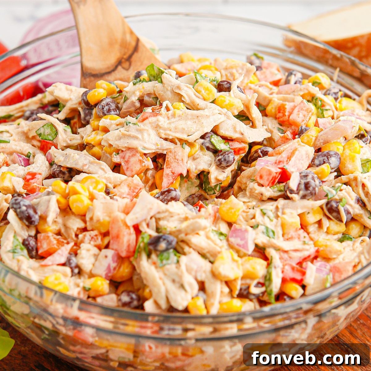 Southwestern Chicken Salad 2 A vibrant Southwest Chicken Salad in a clear glass bowl, featuring a colorful mix of chicken, black beans, corn, and bell peppers, with a wooden spoon resting in the bowl.