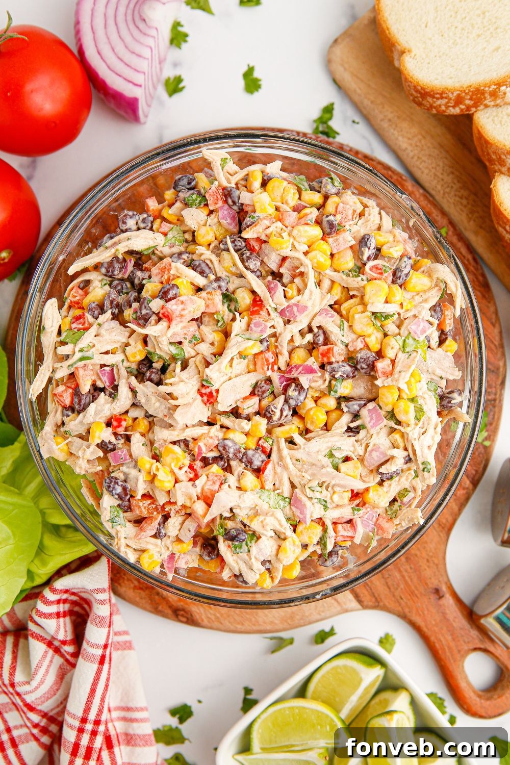 Southwestern Chicken Salad 14 An overhead view of a bowl of Southwest Chicken Salad surrounded by fresh ingredients like onions, tomatoes, lime wedges, and slices of bread, illustrating its components and serving suggestions.