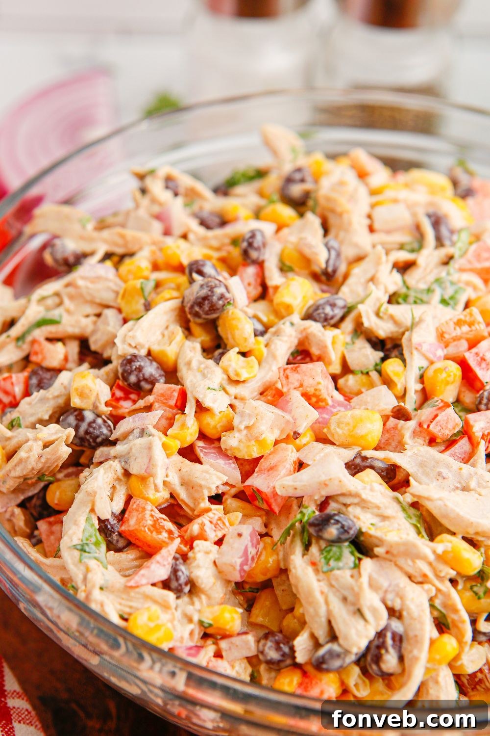 Southwestern Chicken Salad 16 A clean side view of Southwest Chicken Salad served in a transparent glass bowl on a polished wooden table, showcasing its layered textures and appealing colors.