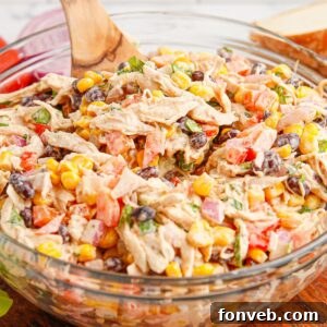 Southwestern Chicken Salad 21 A vibrant Southwest Chicken Salad in a clear glass bowl, featuring a colorful mix of chicken, black beans, corn, and bell peppers, with a wooden spoon resting in the bowl.