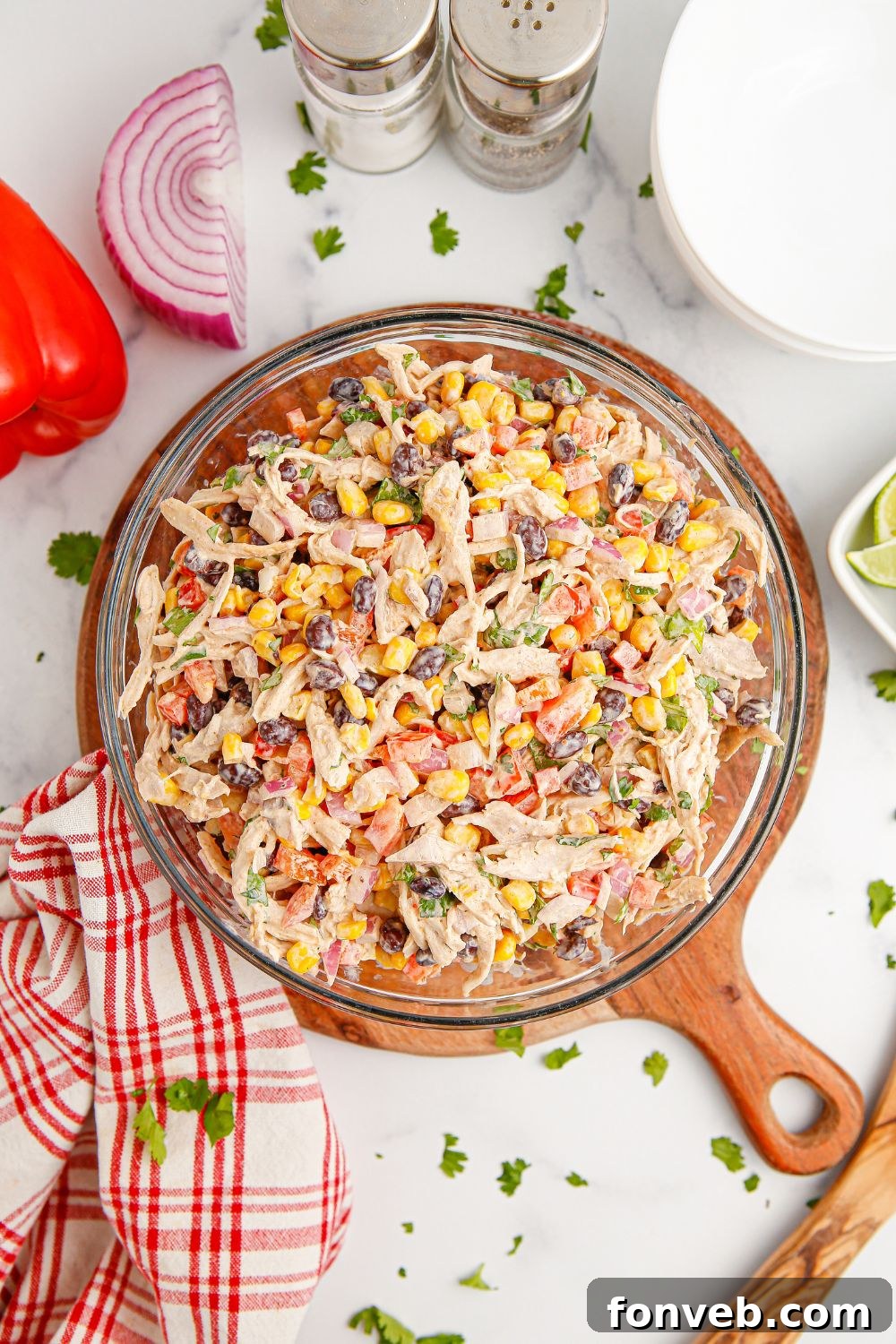 Southwestern Chicken Salad 4 A rustic setup featuring Southwest Chicken Salad in a bowl, flanked by salt and pepper shakers, a patterned towel, and fresh vegetables, highlighting its wholesome appeal.