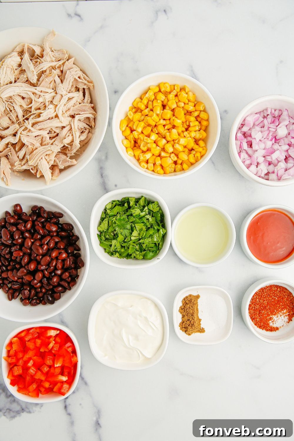 Southwestern Chicken Salad 5 Assorted fresh ingredients for Southwest Chicken Salad, including black beans, corn, diced bell peppers, and onions, neatly arranged in small bowls on a sleek marble counter, showcasing their readiness for preparation.
