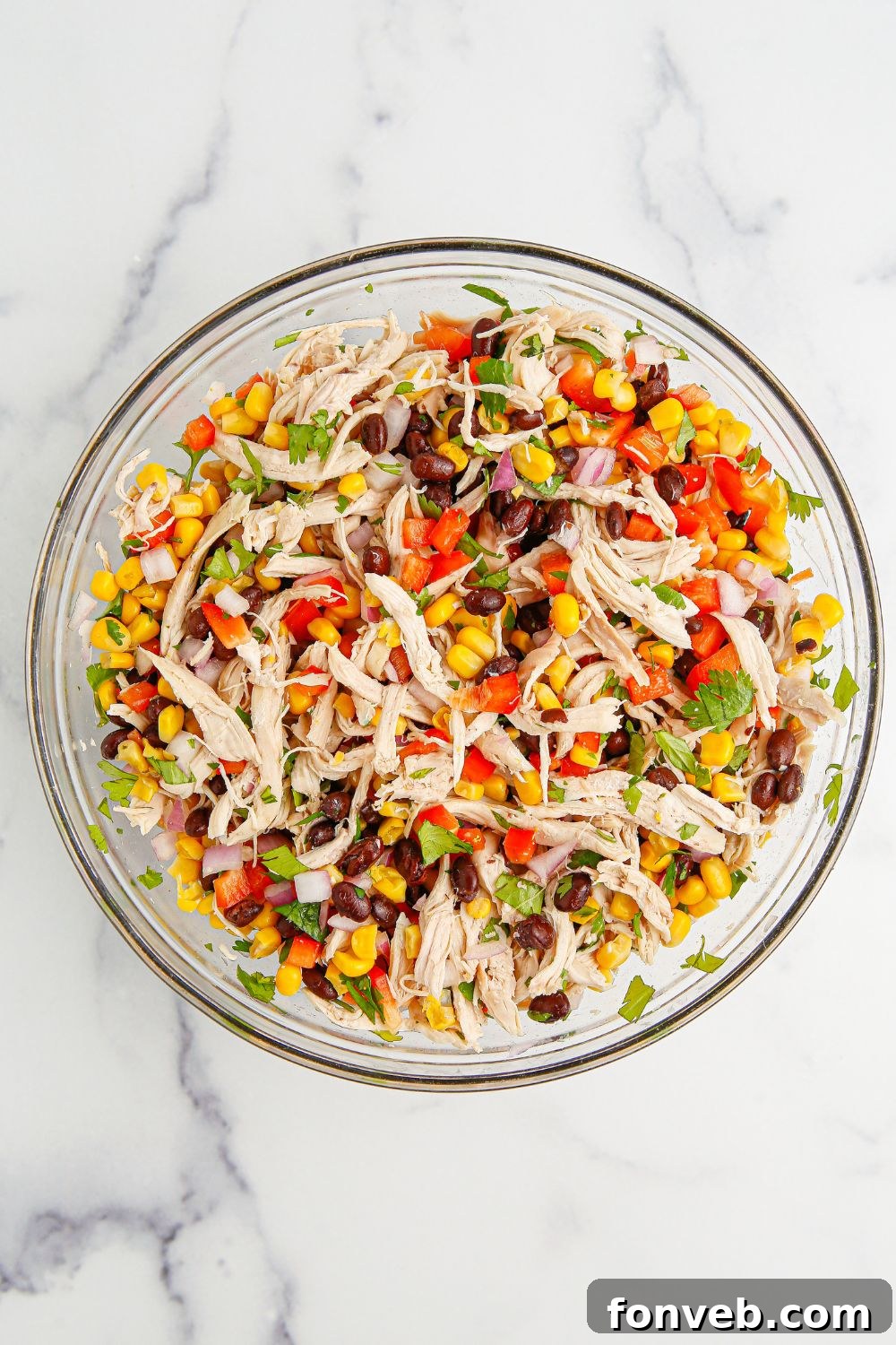 Southwestern Chicken Salad 7 Southwest Chicken Salad ingredients lightly tossed in a bowl, showing the initial mixing of chicken, beans, and vegetables before the dressing is fully incorporated.