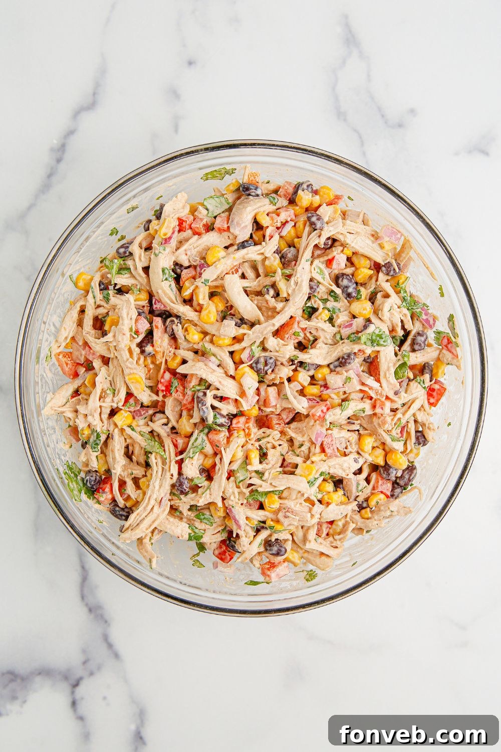 Southwestern Chicken Salad 10 The finished Southwest Chicken Salad, thoroughly mixed and presented in a large glass bowl on a wooden table, showcasing its uniform texture and inviting appearance.