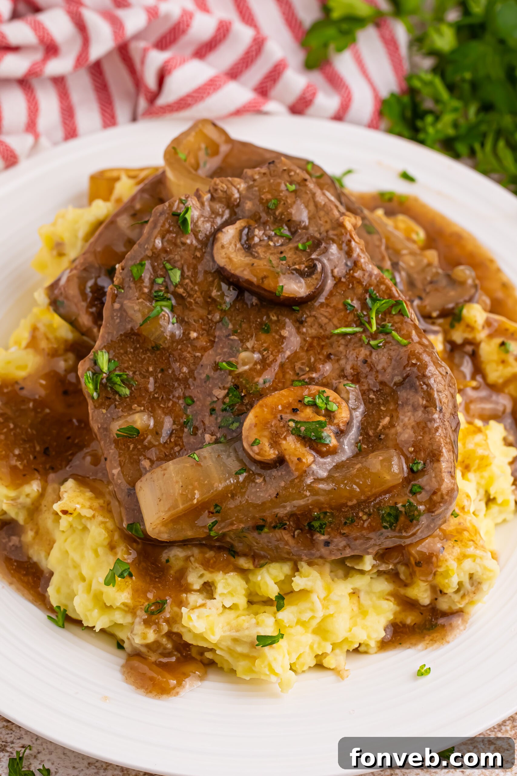 plate with a spread of mashed potatoes topped with steak, onions and mushroom gravy. There is a crock pot in the background