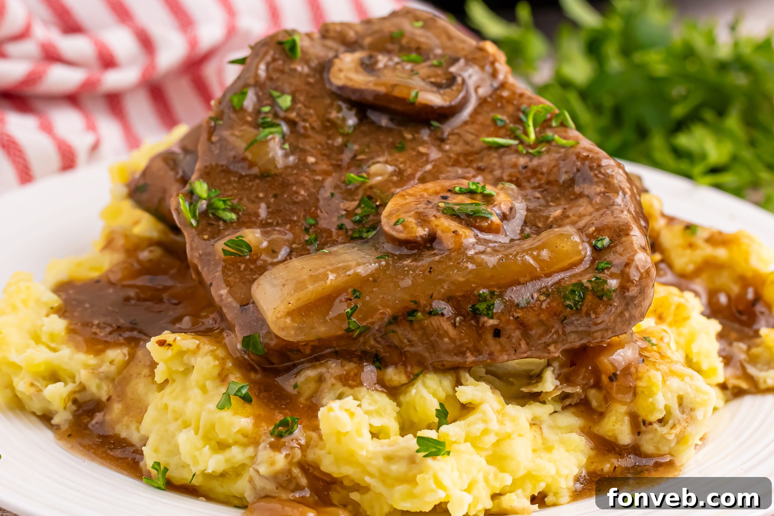 Slow Cooker Round Steak and Gravy on a plate with a bed of mashed potatoes under the steak and gravy