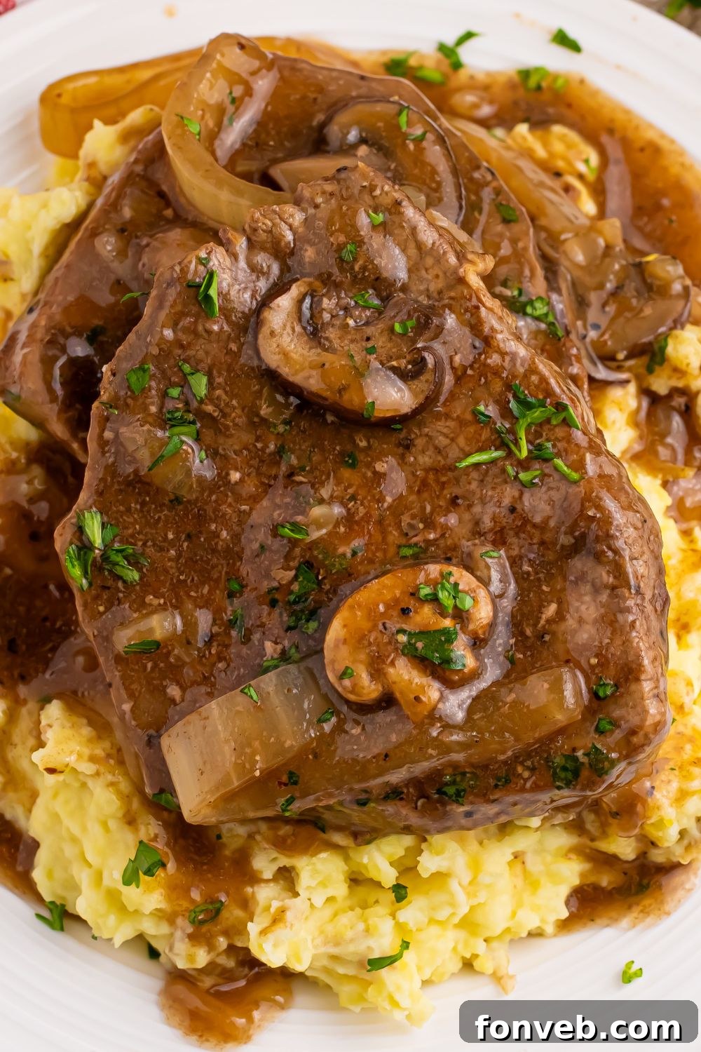 Slow Cooker Round Steak and Gravy on a plat with mashed potatoes under the steak