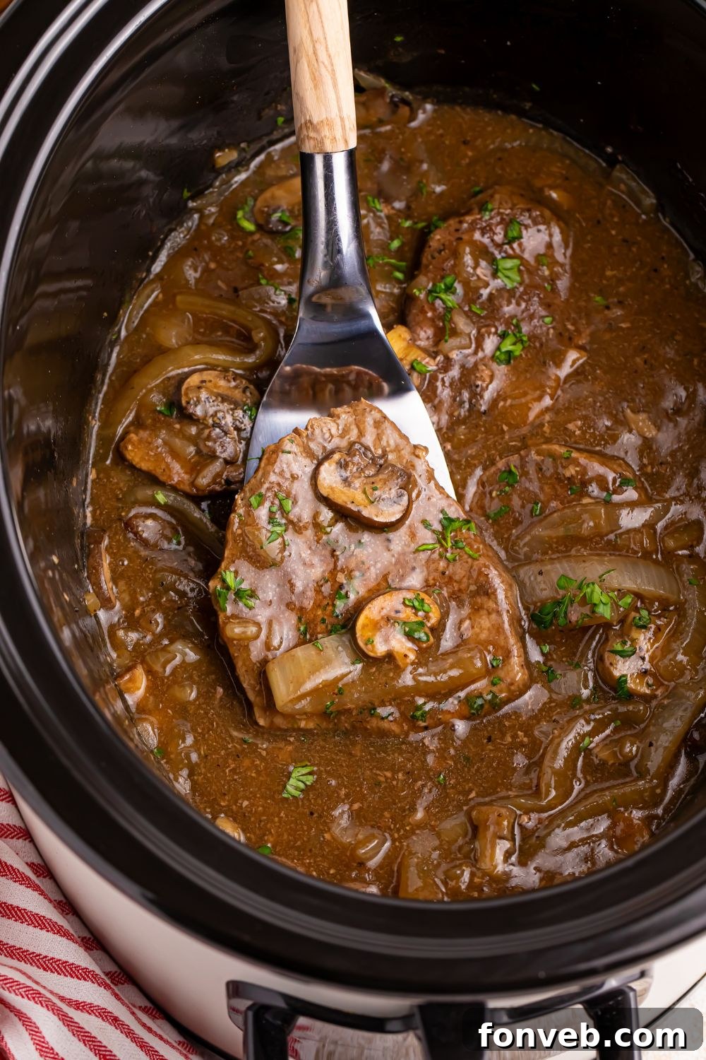 steak and gravy in slow cooker with a spatula with one of the steaks on it being lifted out of the crockpot