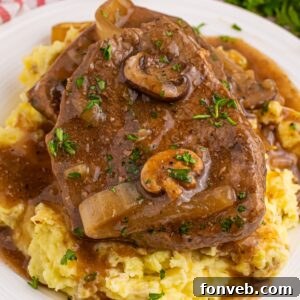 Slow Cooker Round Steak and Gravy on a plate with a bed of mashed potatoes under the steak and gravy