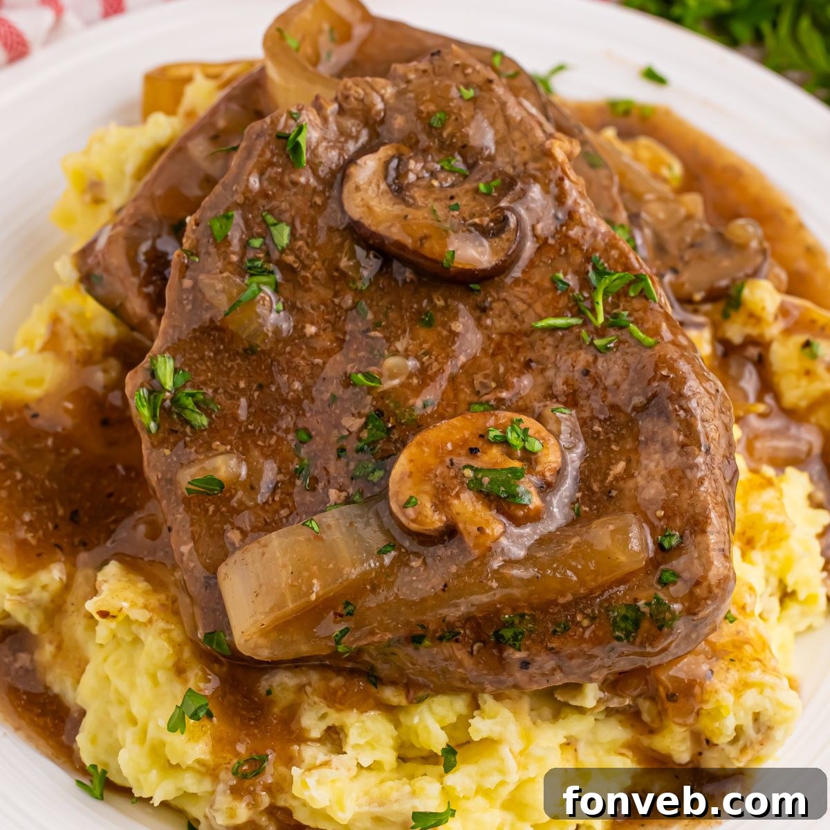 Slow Cooker Round Steak and Gravy on a plate with a bed of mashed potatoes under the steak and gravy