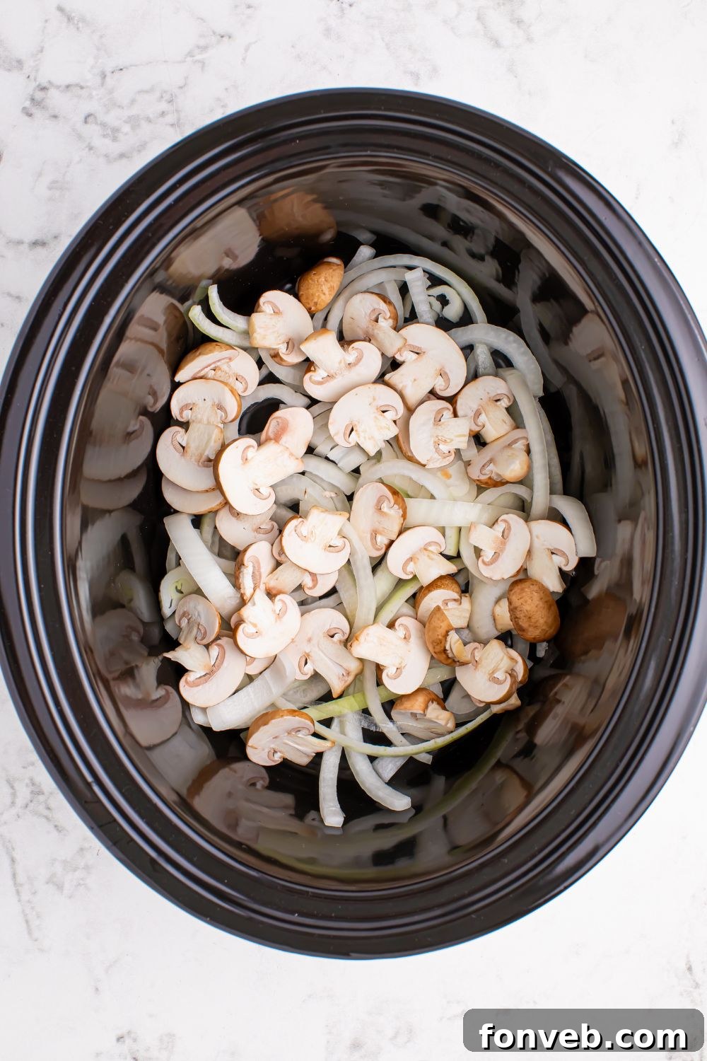 mushrooms and onions in a crockpot sitting on the table 