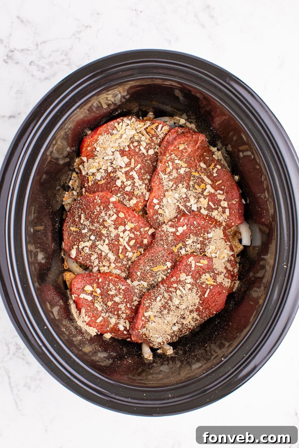 slow cooker with round steak topped with an onion soup mix spread over the meat 