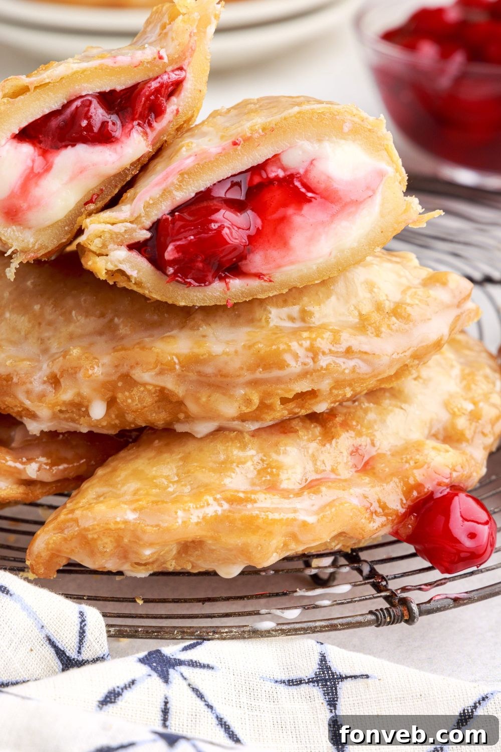 Cherry Cheesecake Hand Pies on a cooling rack stancked on top of each other, with one cut in half to show the sweet filling inside of cream cheese and cherries 