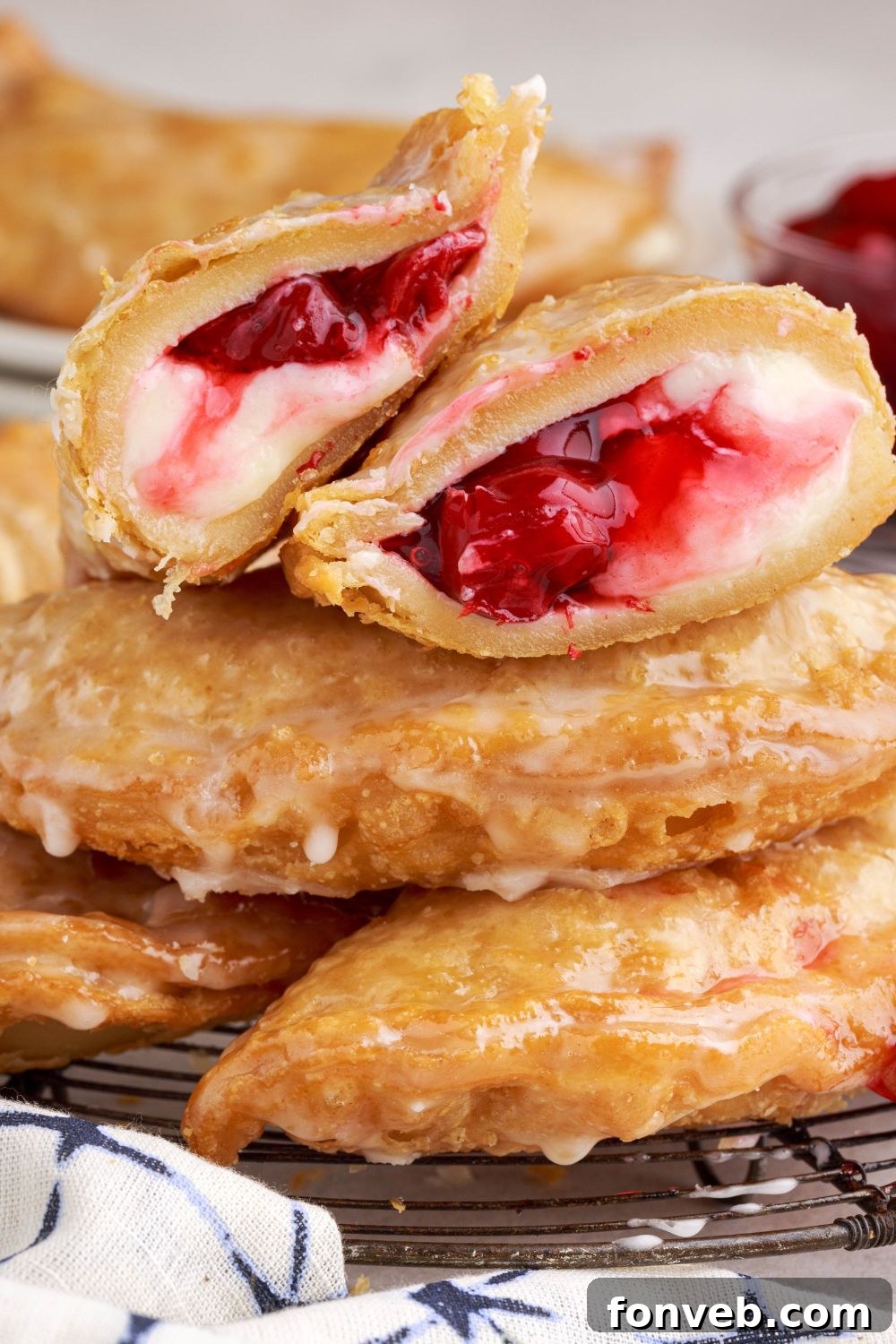Cherry Cheesecake Hand Pies on table with one sliced in half sitting on top of the stack