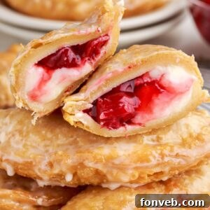 Cherry Cheesecake Hand Pies stacked on table with on cut in half to show the filling