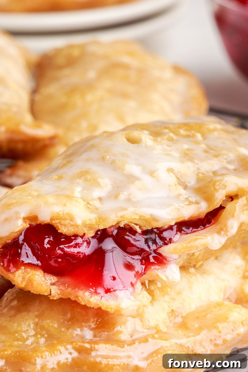 Cherry Cheesecake Hand Pies stacked on top of each other. One of the hand pies has some of the cherry pie filling showing on the edge of the crust 