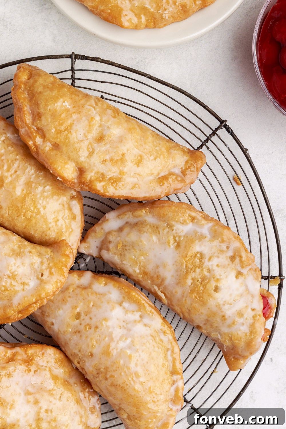 Cherry Cheesecake Hand Pies on a metal cooling rack sitting on table with bowls of ingredients around the cooling rack 