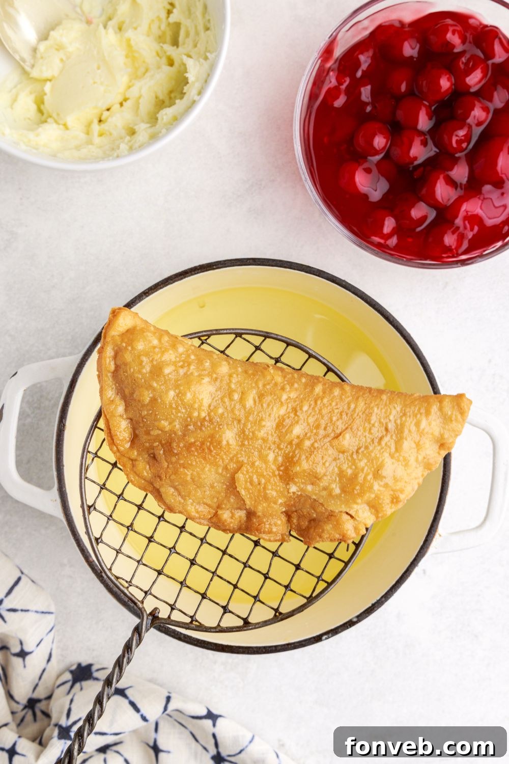 slotting spoon holding a fried Cherry Cheesecake Hand Pies over a pan of oil